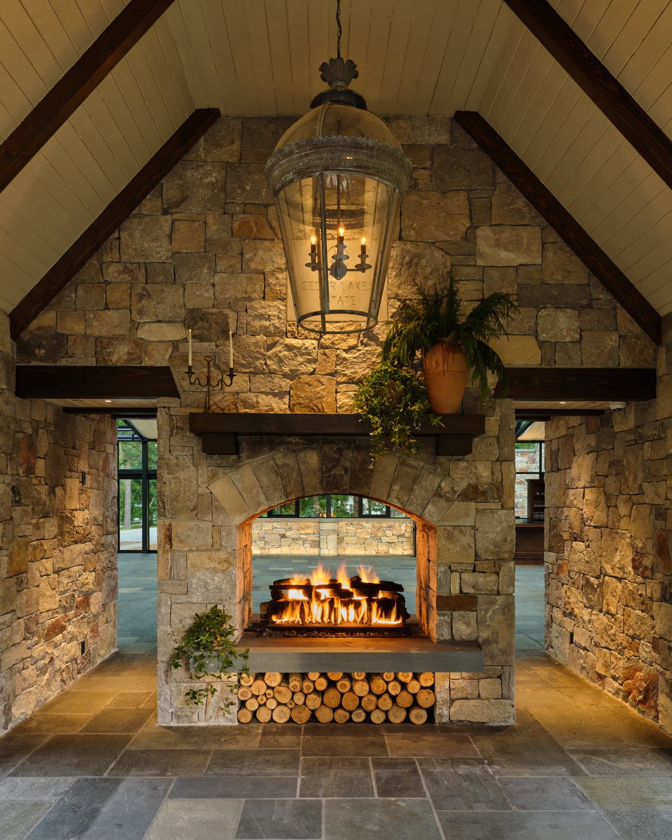 Inside the entry gable: the stone fireplace under the timber rafters, a lantern hanging from the ridge