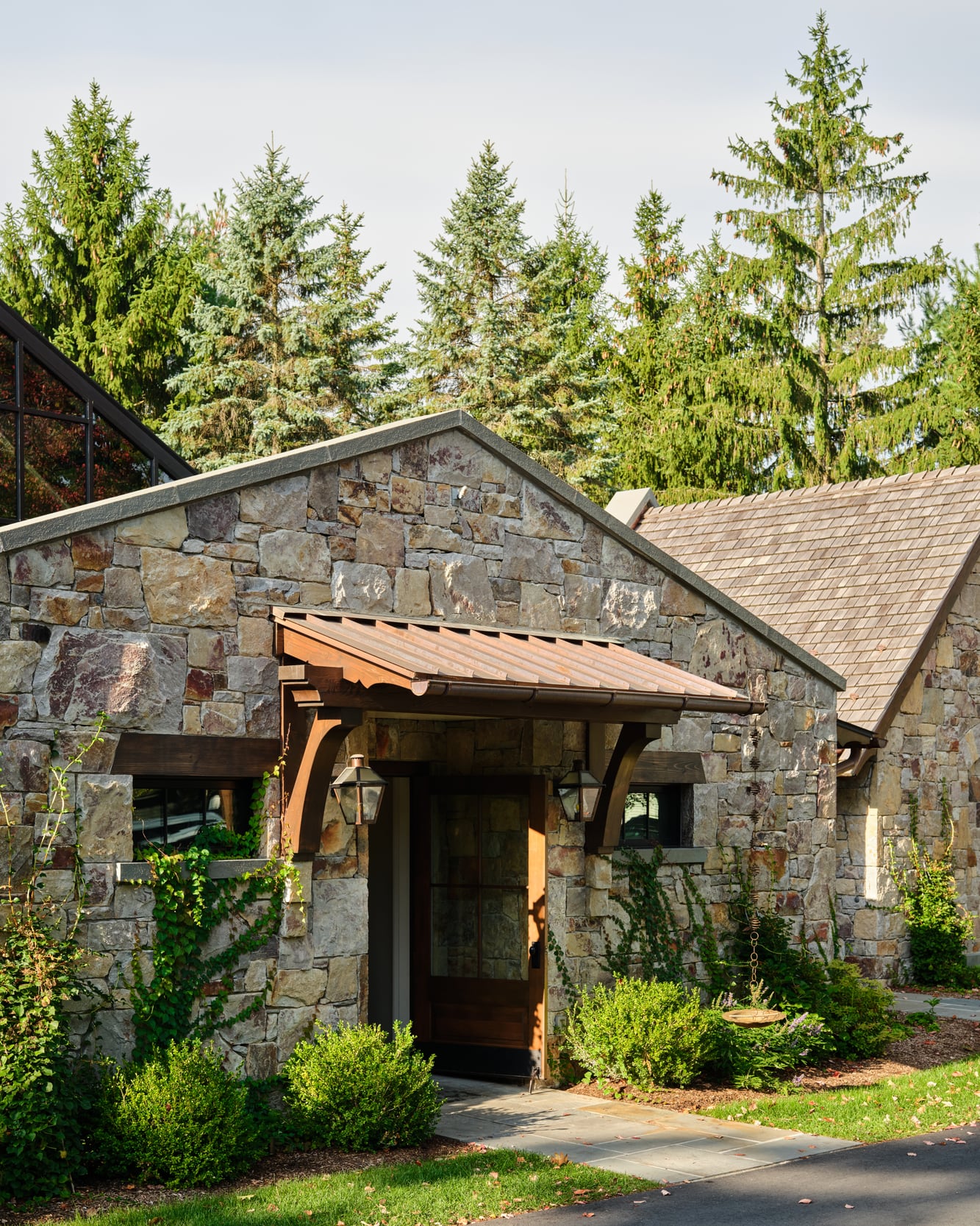 The rear porch on its timber brackets, stone walls and spruce behind
