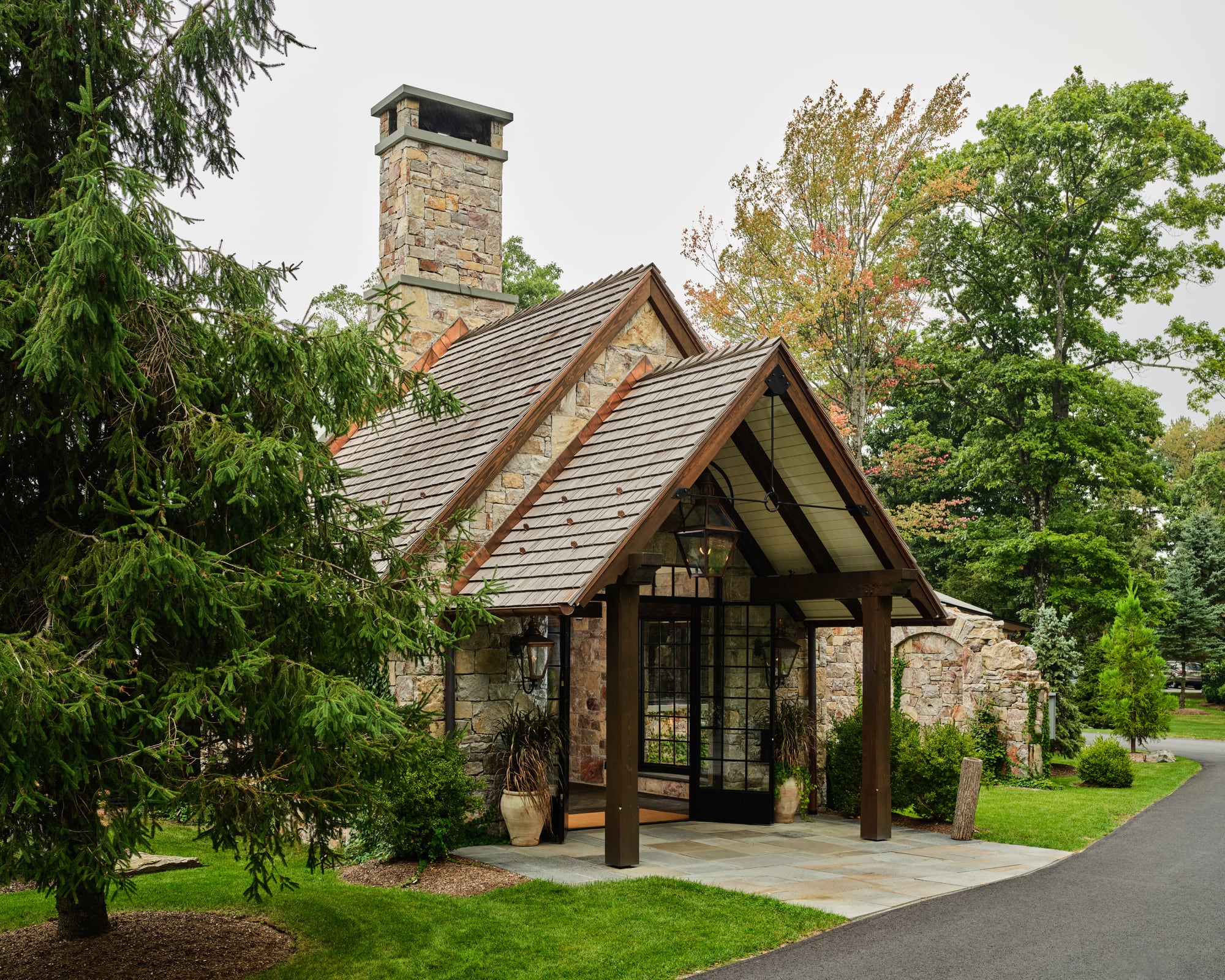 The Glasshouse from the side: stone walls and chimney, the timber entry gable and the glass roof among the trees