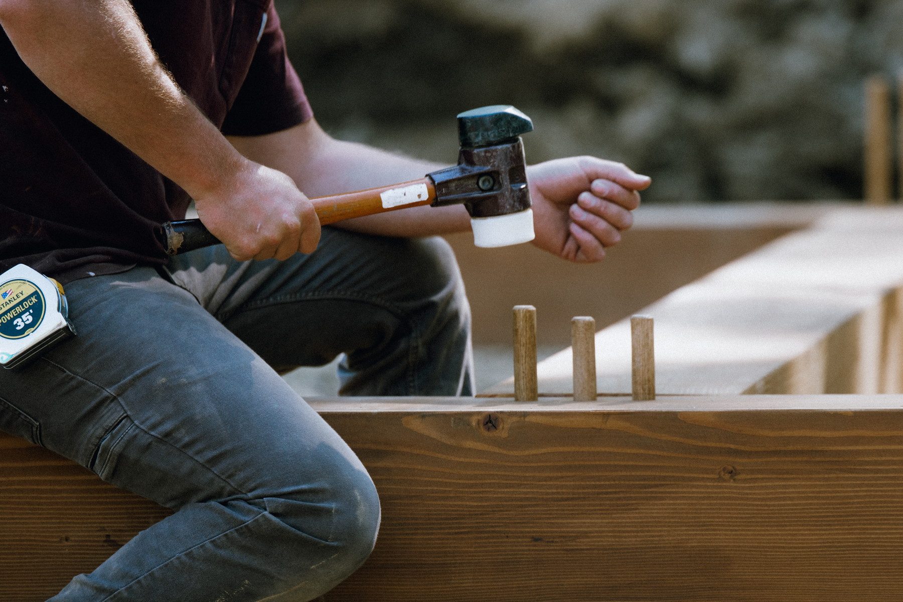A framer with a mallet driving pegs into a mortise and tenon joint