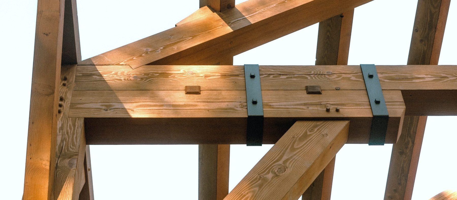 Steel strap brackets around a built-up beam where it meets a post, braces crossing behind