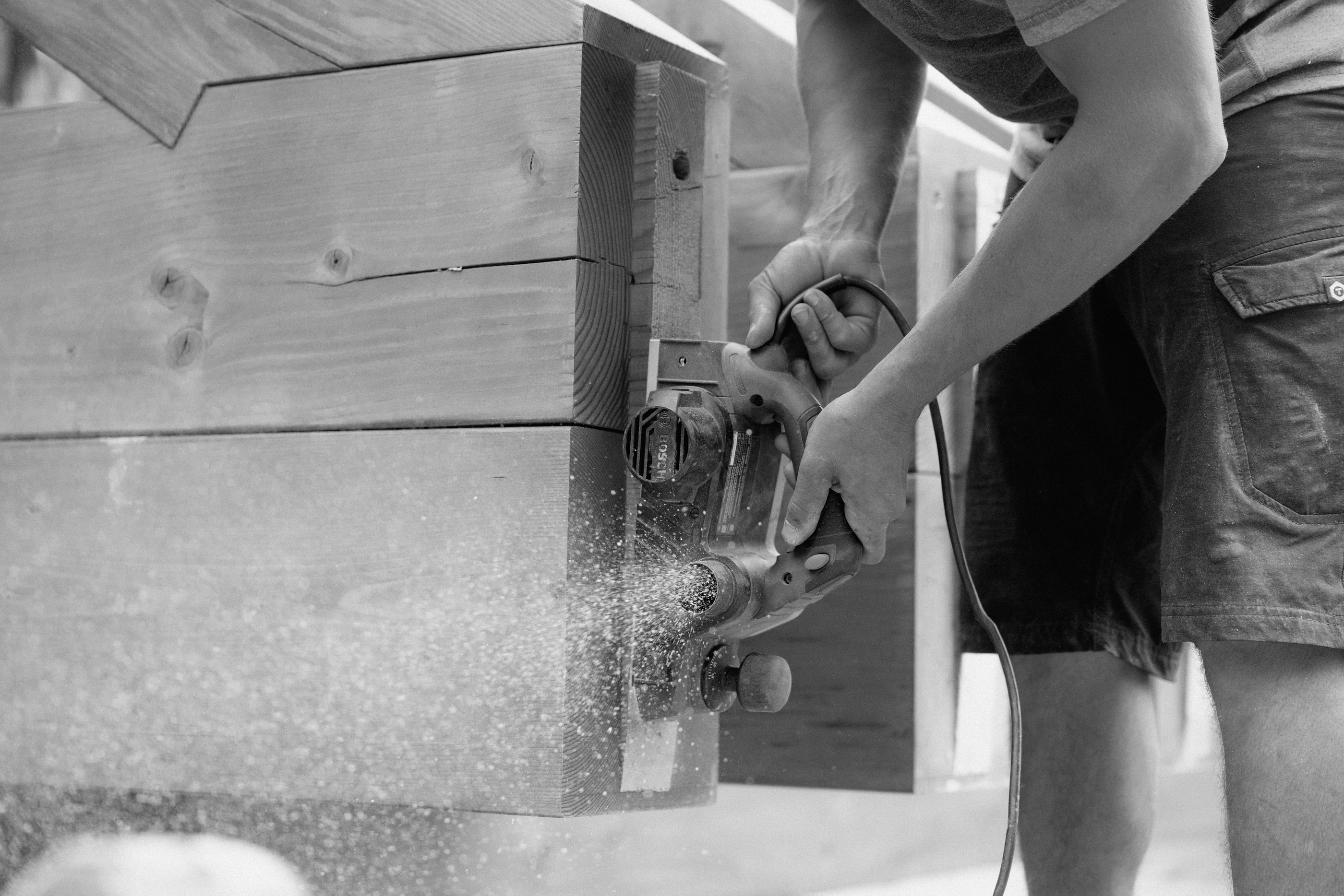 A crew member cutting a timber with a circular saw, sawdust flying, black and white