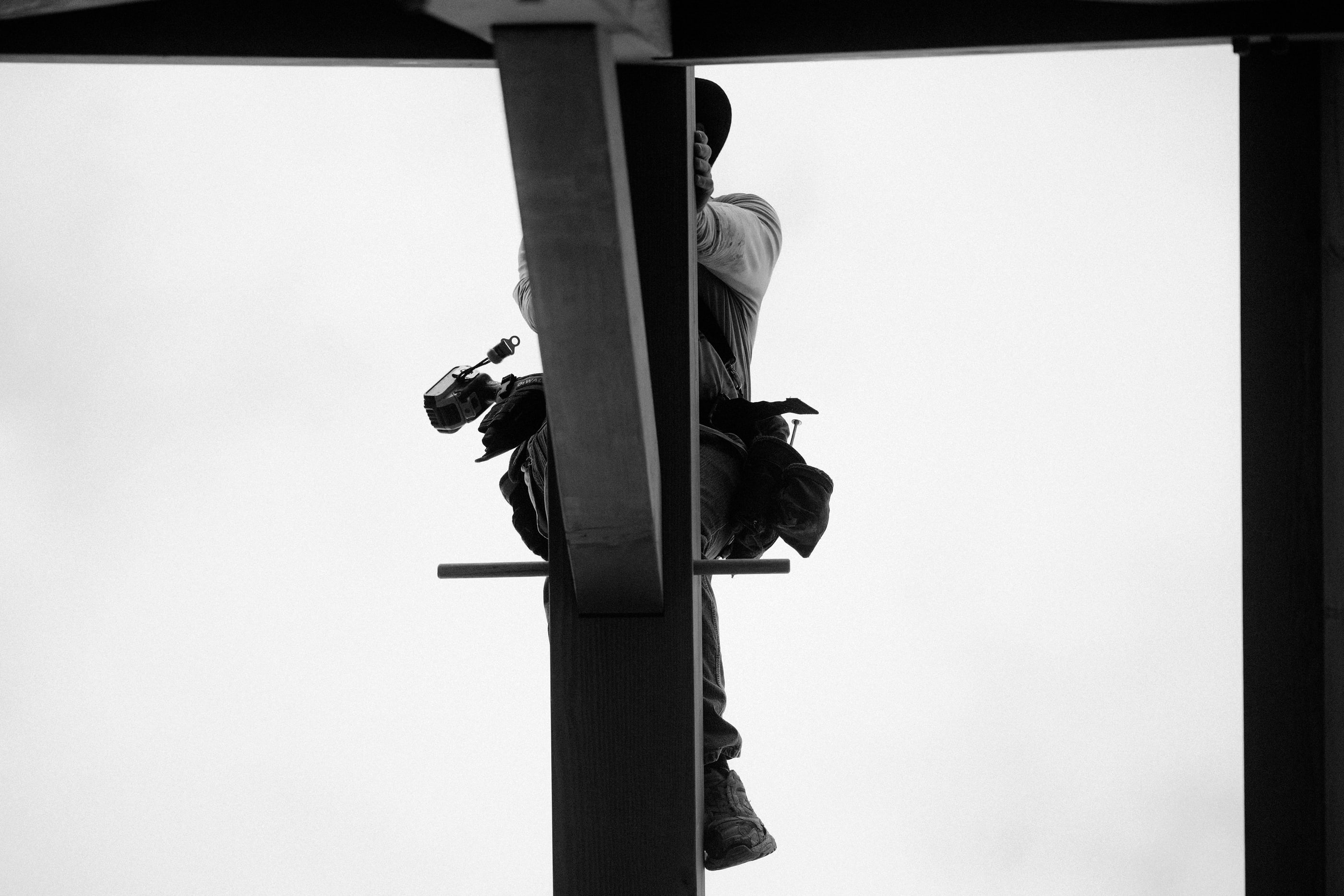 A crew member working near the ridge, tools on his belt, against an open sky, black and white