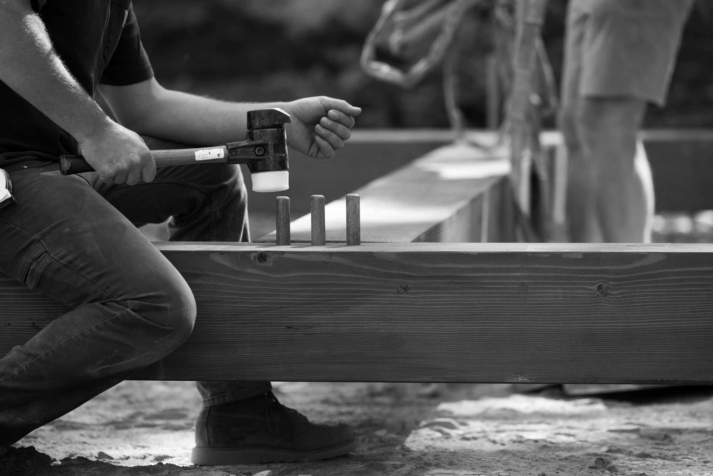 Driving pegs into a mortised beam with a mallet, black and white