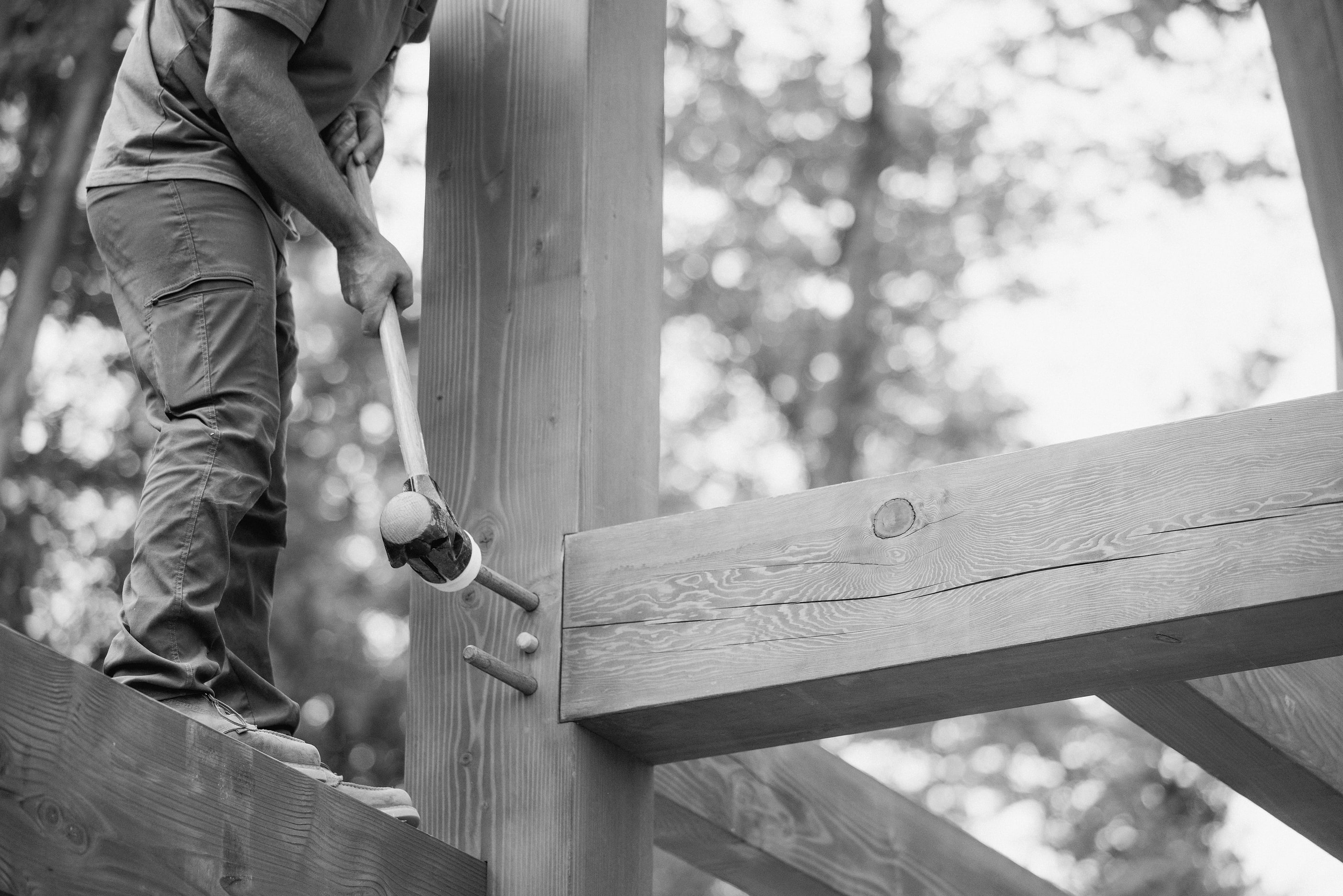 A crew member setting pegs at a beam connection with a mallet, black and white