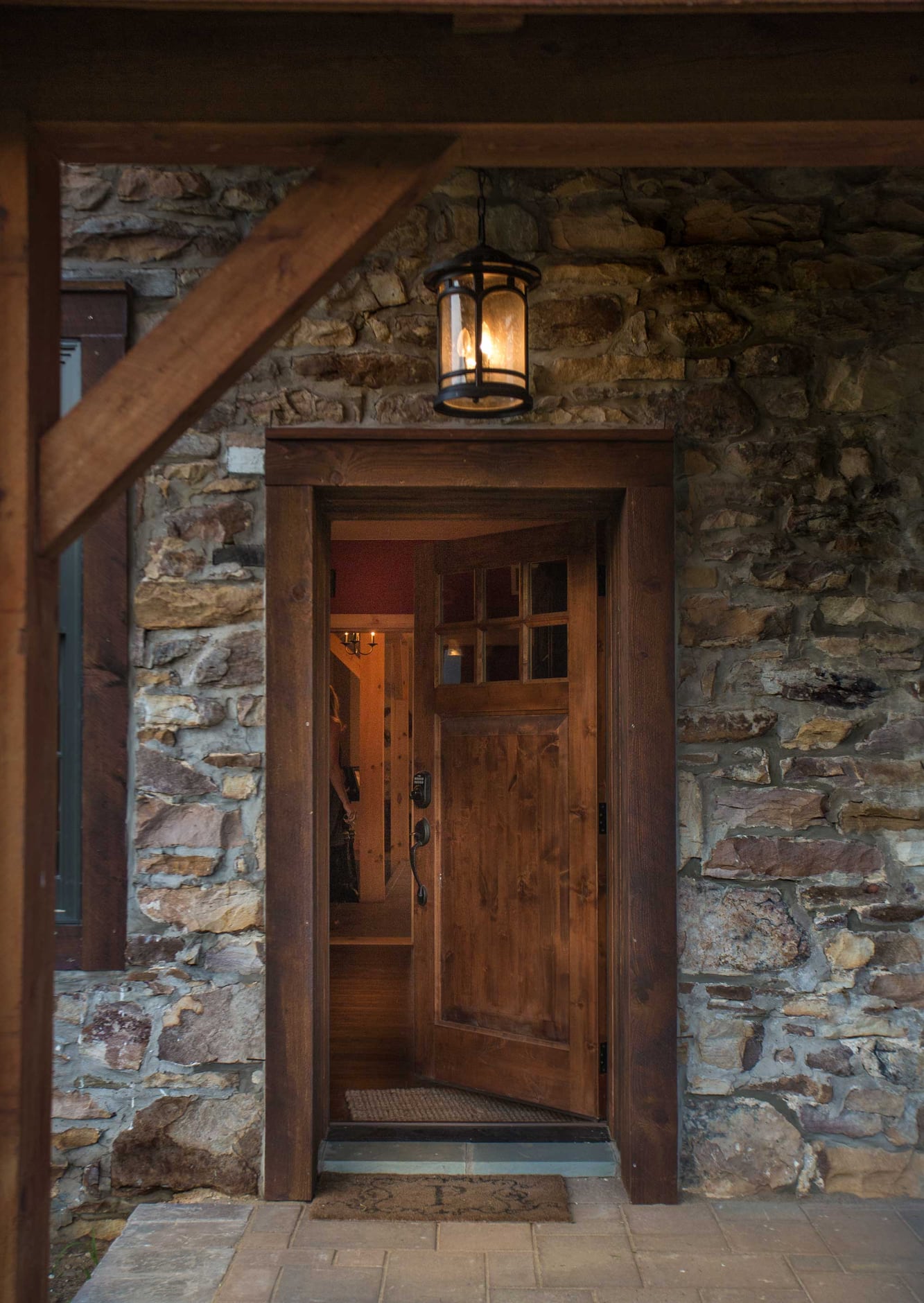 The front door in the old stone wall, a lantern overhead and a porch brace at the left