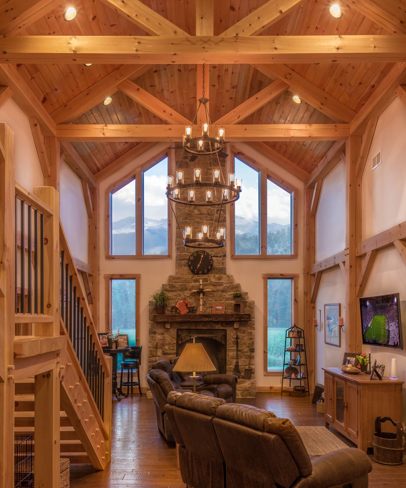 The great room addition: king post trusses under a pine ceiling, a stone chimney between tall windows, mountains beyond