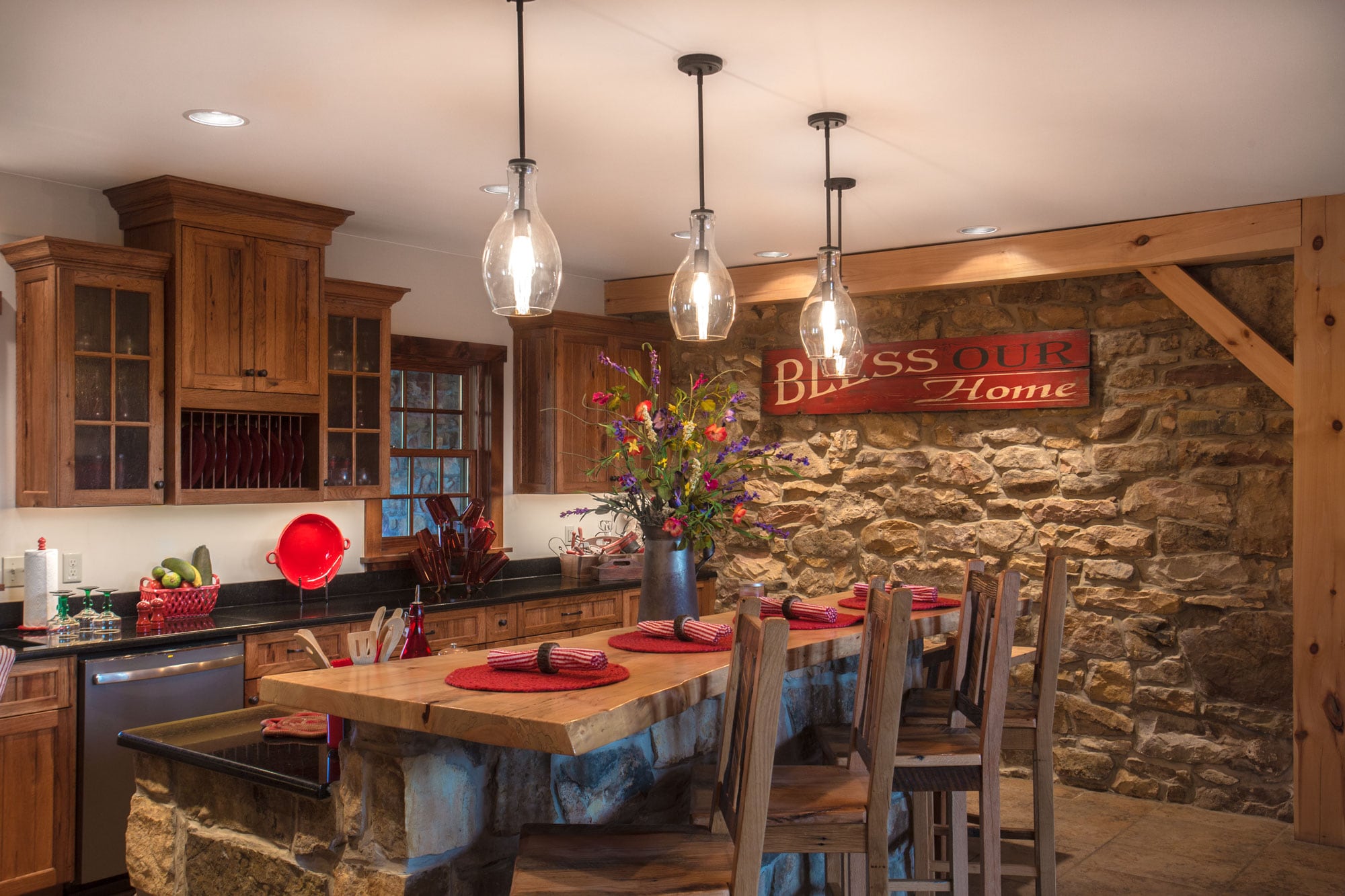 The kitchen: a timber post and braced beam framing the old stone wall, pendants over a live-edge counter