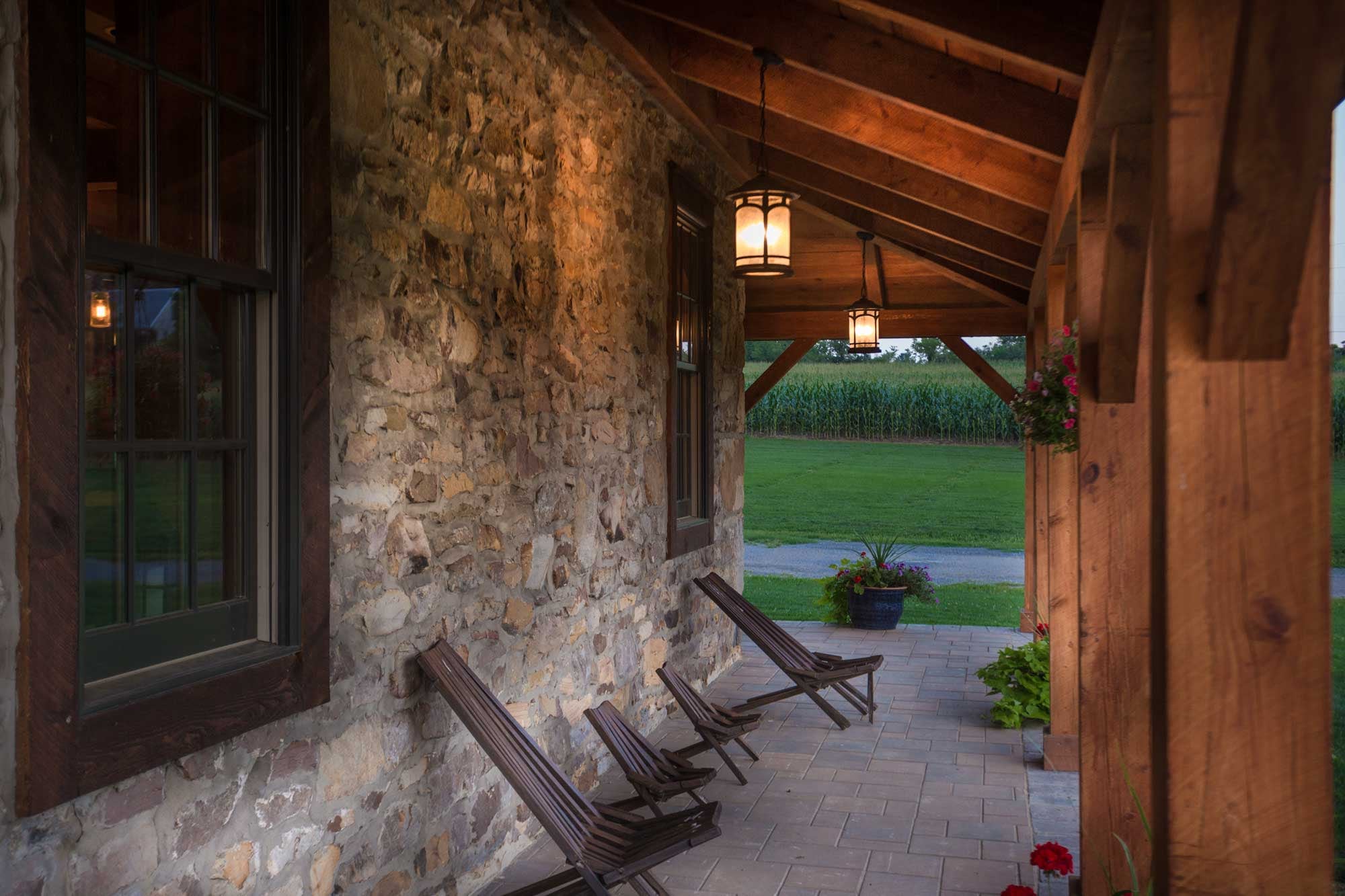 Chairs along the stone wall under the porch, lanterns lit, the cornfield beyond
