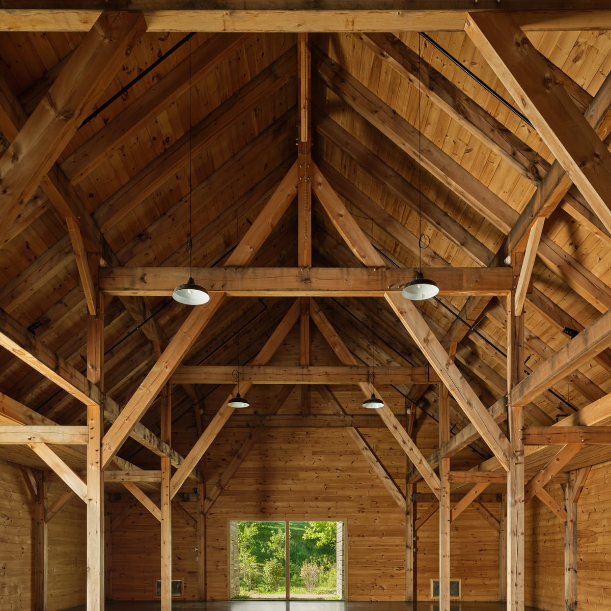 Down the center aisle of the INNESS barn, anchor beams and sling braces overhead, the far doors open to the field