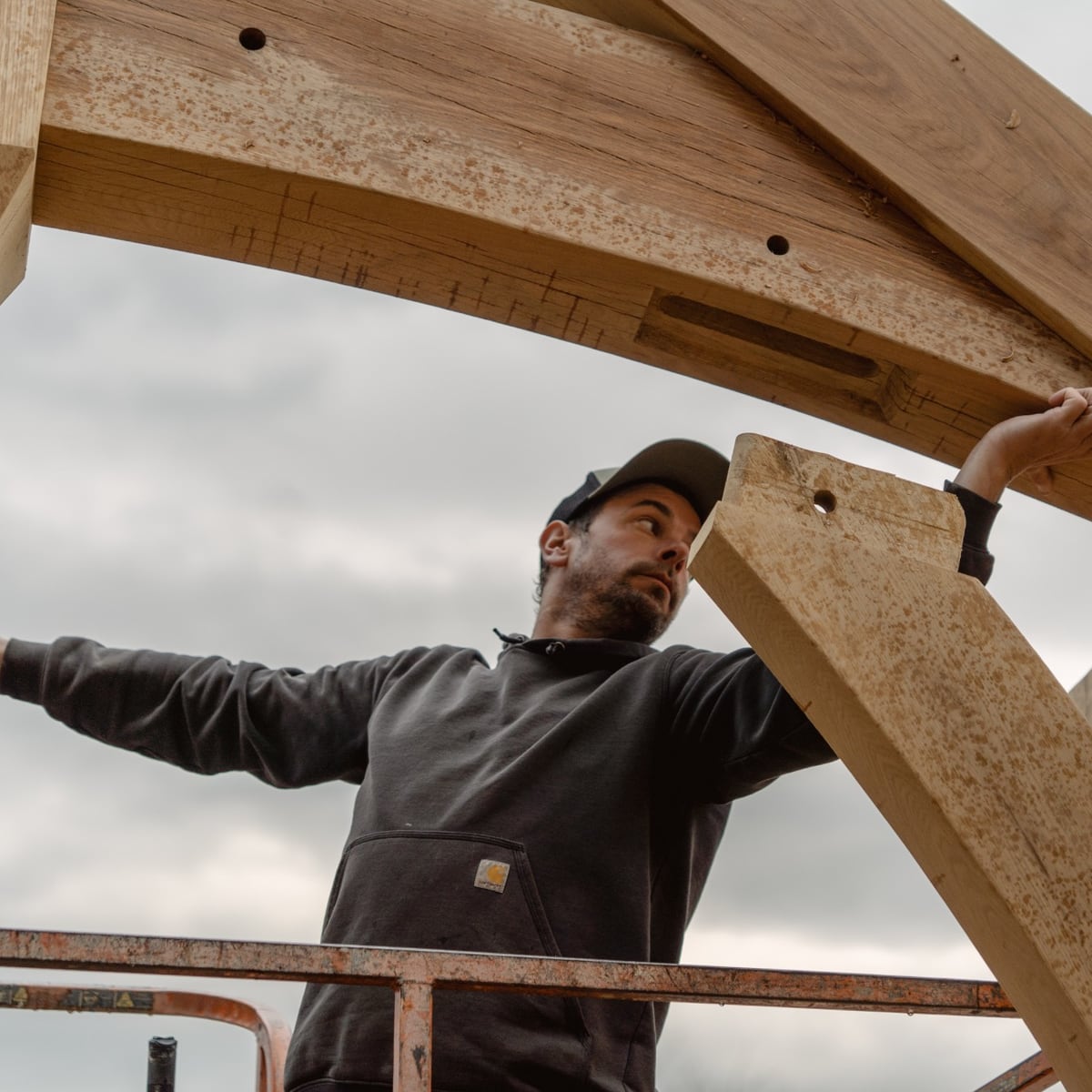 A framer on a lift guiding a white oak brace into its arched timber