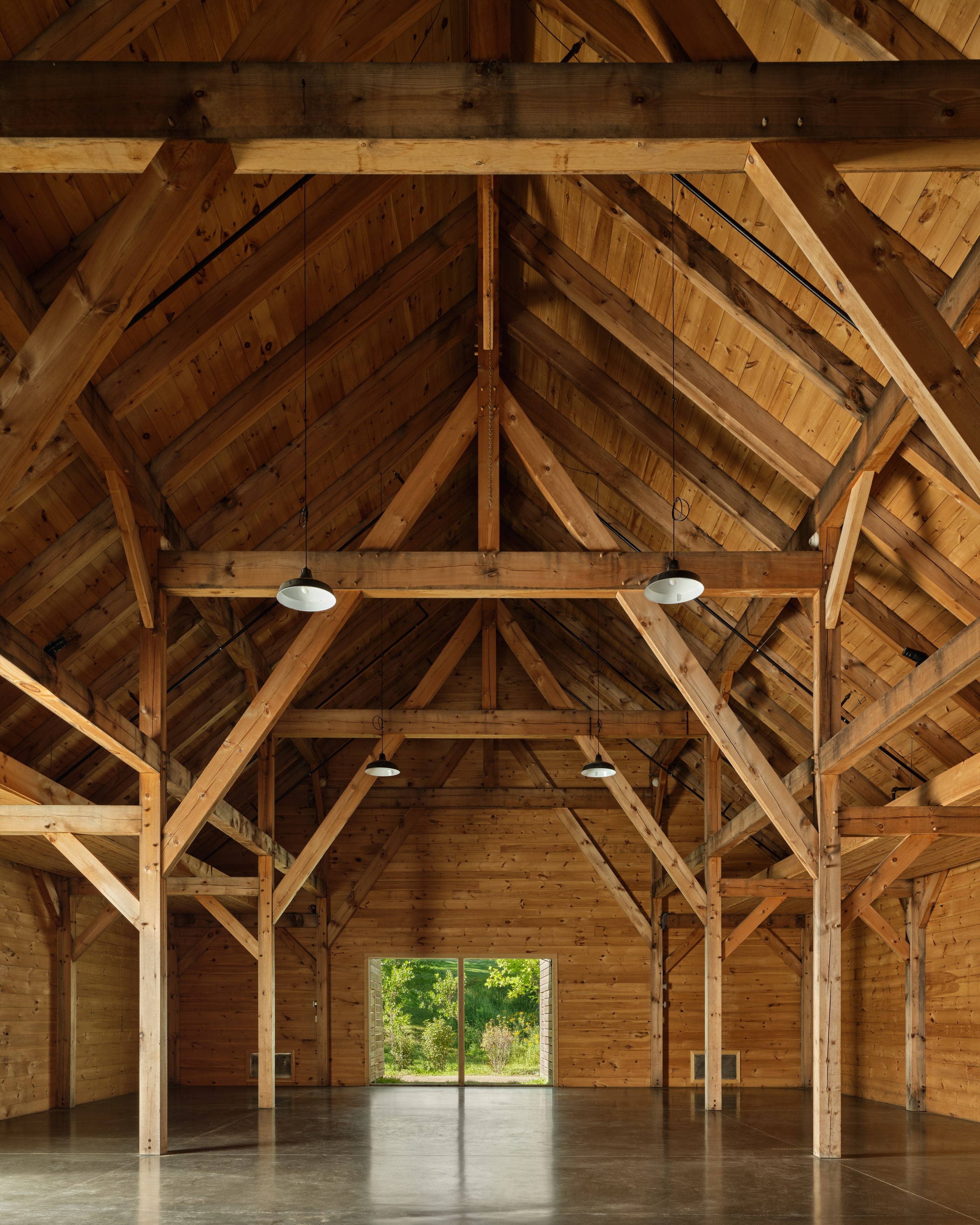 Down the center aisle of the finished barn, anchor beams and sling braces overhead, the far doors open to the field