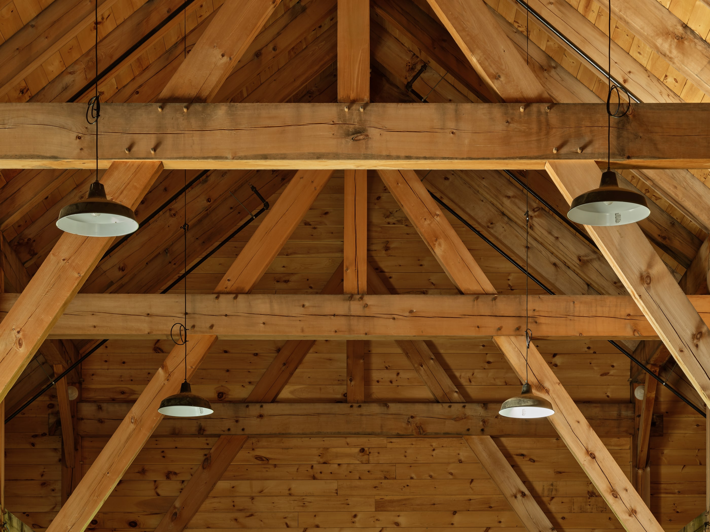 The anchor beams and sling braces from below, their wedged through-tenons showing at the posts, pendant lights hung between