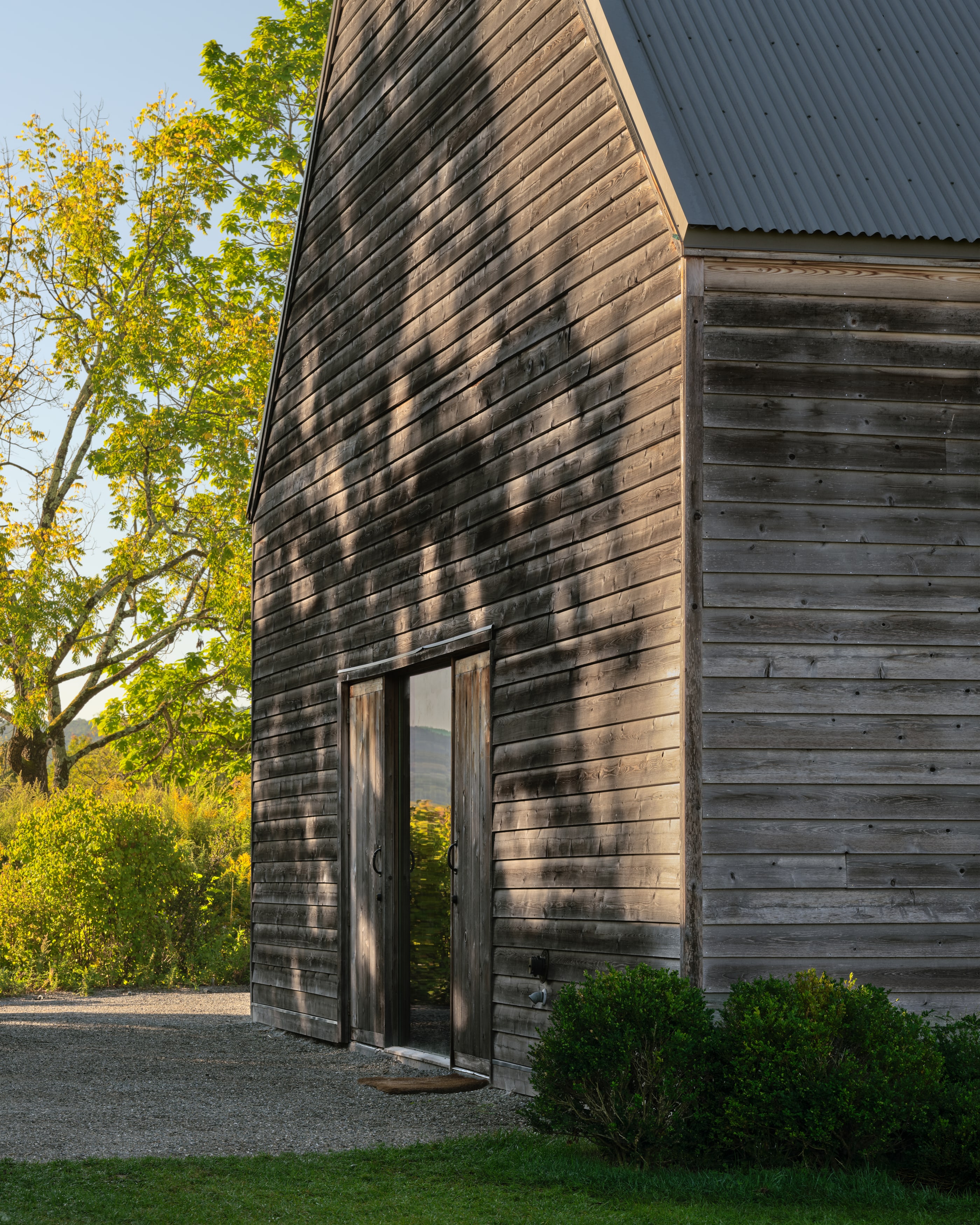 The gable end at evening, tree shadows across the siding and the doors open to the view