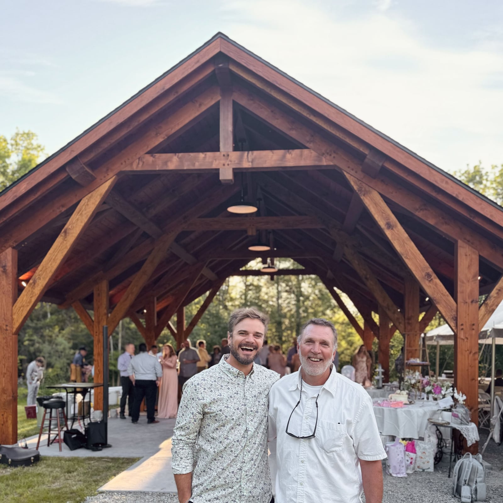 Kayle Sickler and his dad, both laughing, in front of a finished timber frame pavilion during a celebration