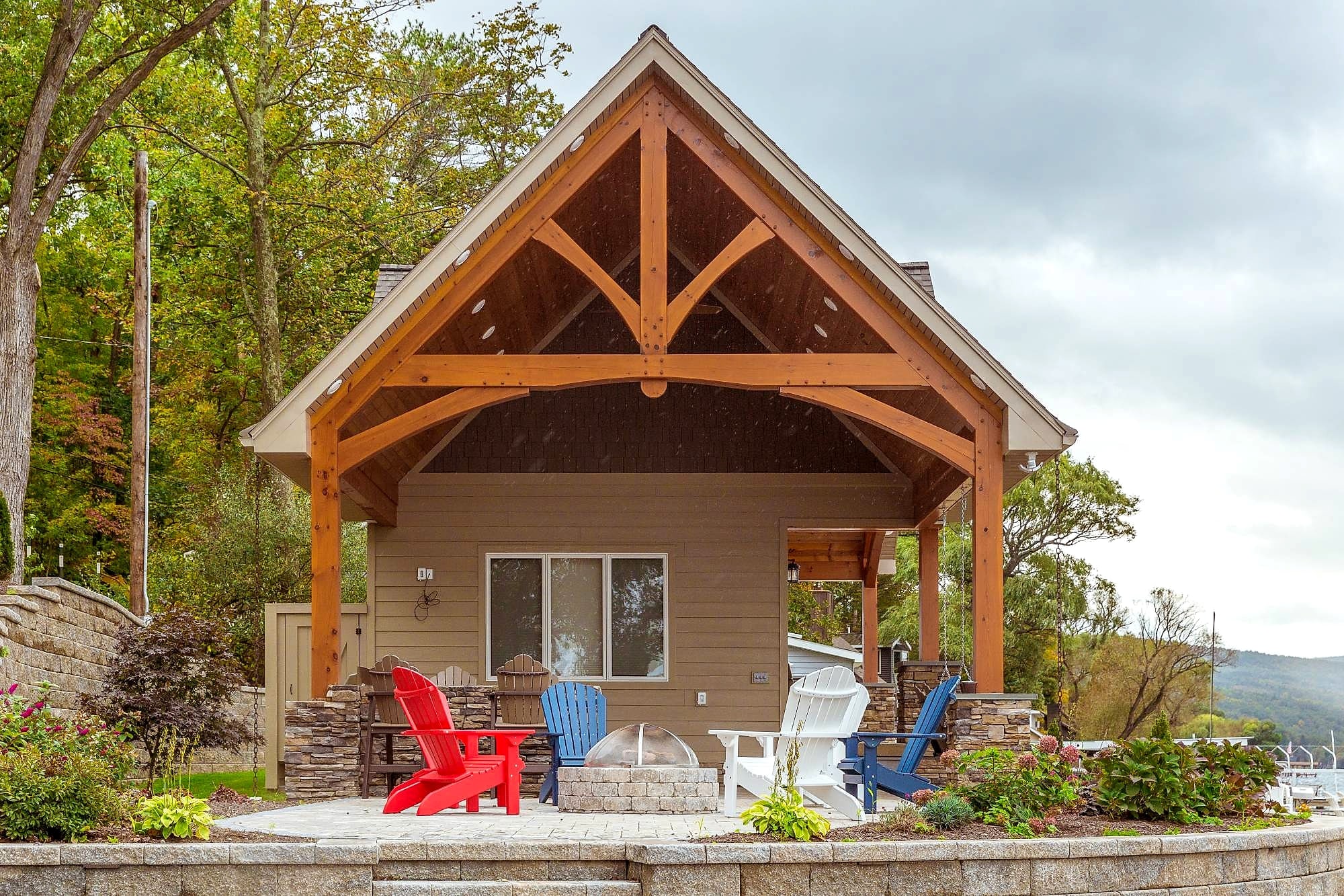 The cabana straight on: its timber bents, and red, white, and blue Adirondack chairs around the fire pit