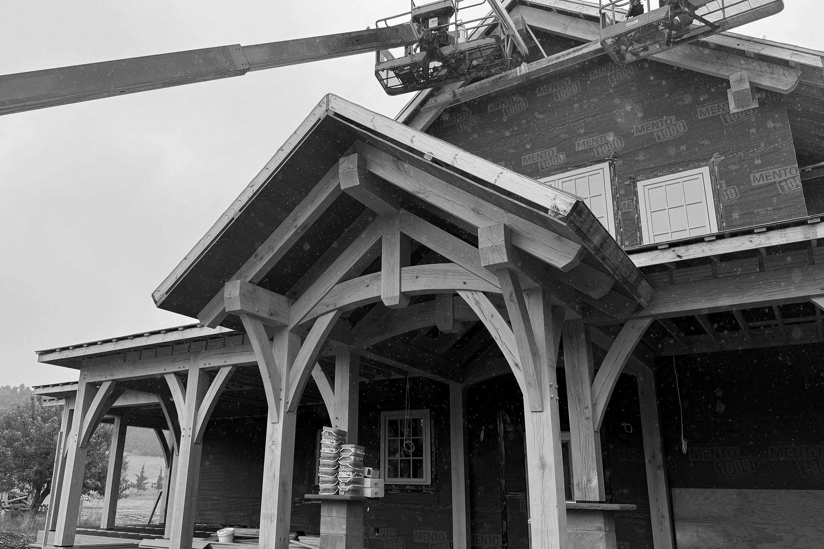 The white oak front porch, its gable braced with curved timbers, two lifts working on the roof above in the rain, black and white