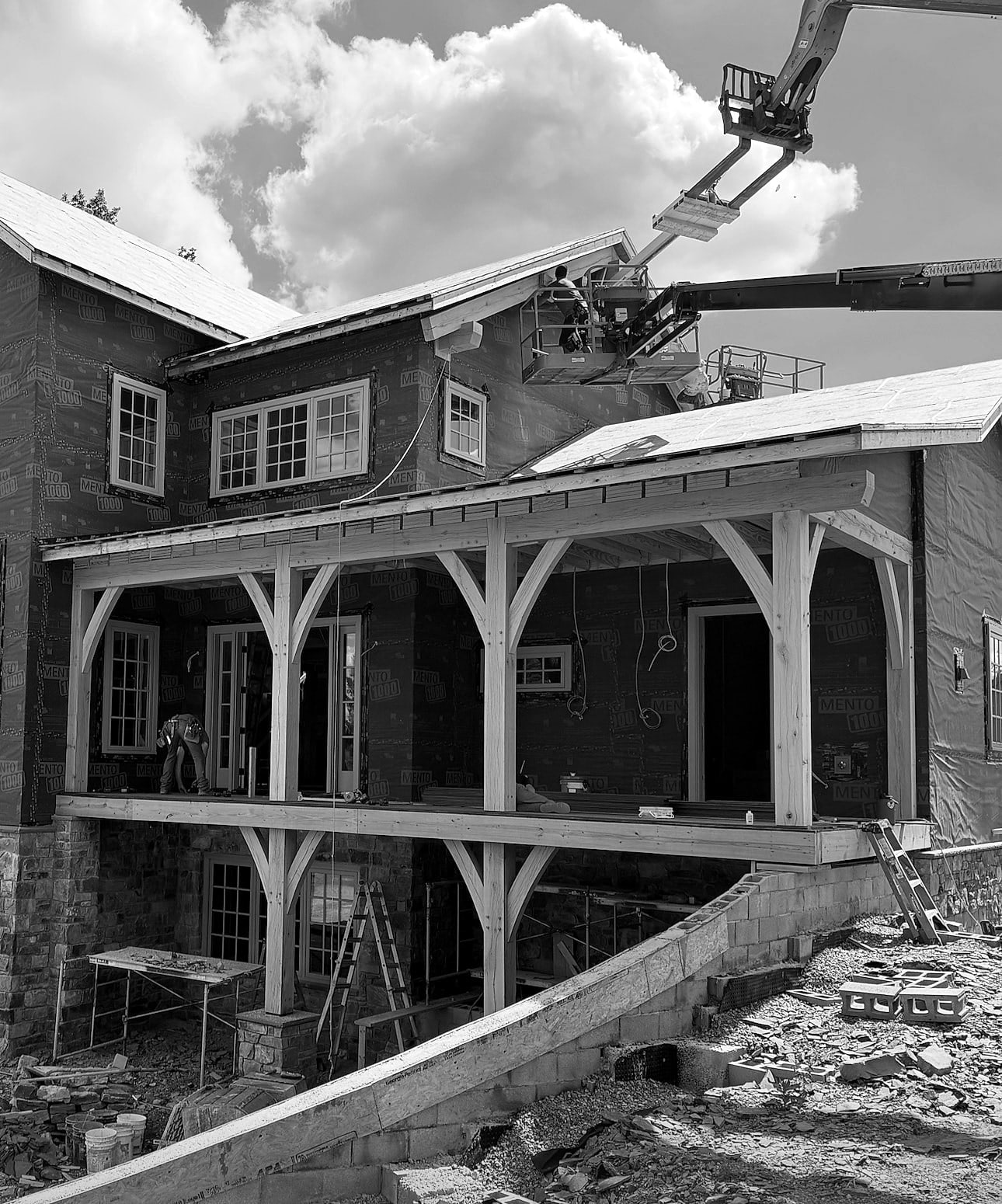 A white oak porch standing against the house wrap while the roof goes on, black and white