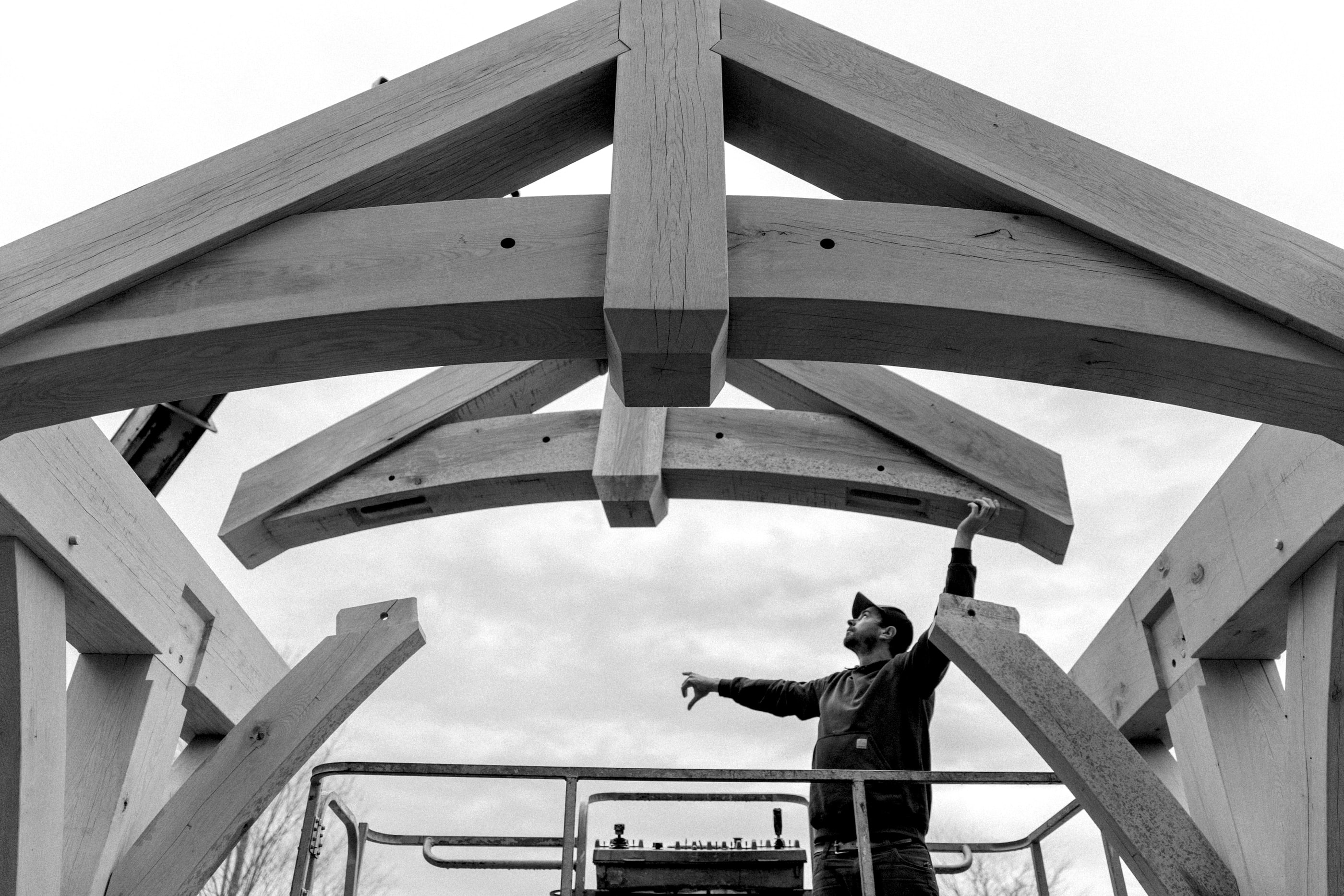 A crew member on a lift guiding an arched truss into place, black and white