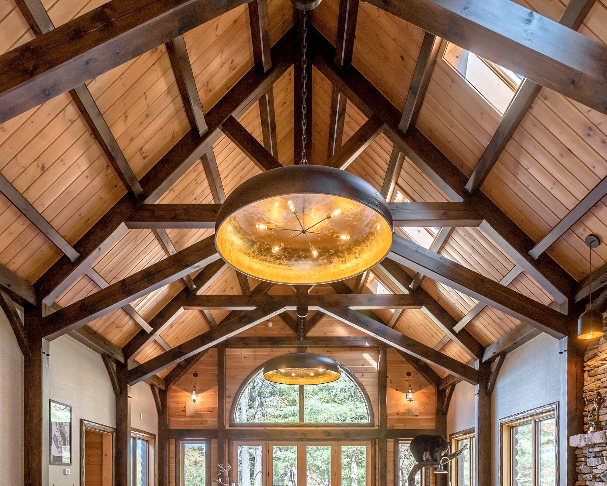 The great room's timber trusses over the arched window, pendant lights hung from the ridge
