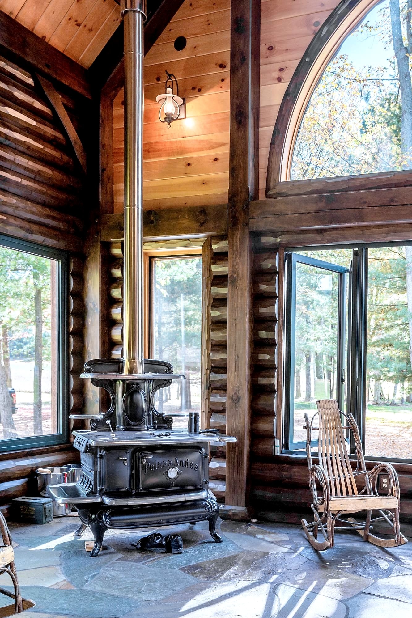 An antique cook stove beneath the arched window in the log-walled room, flagstone floor