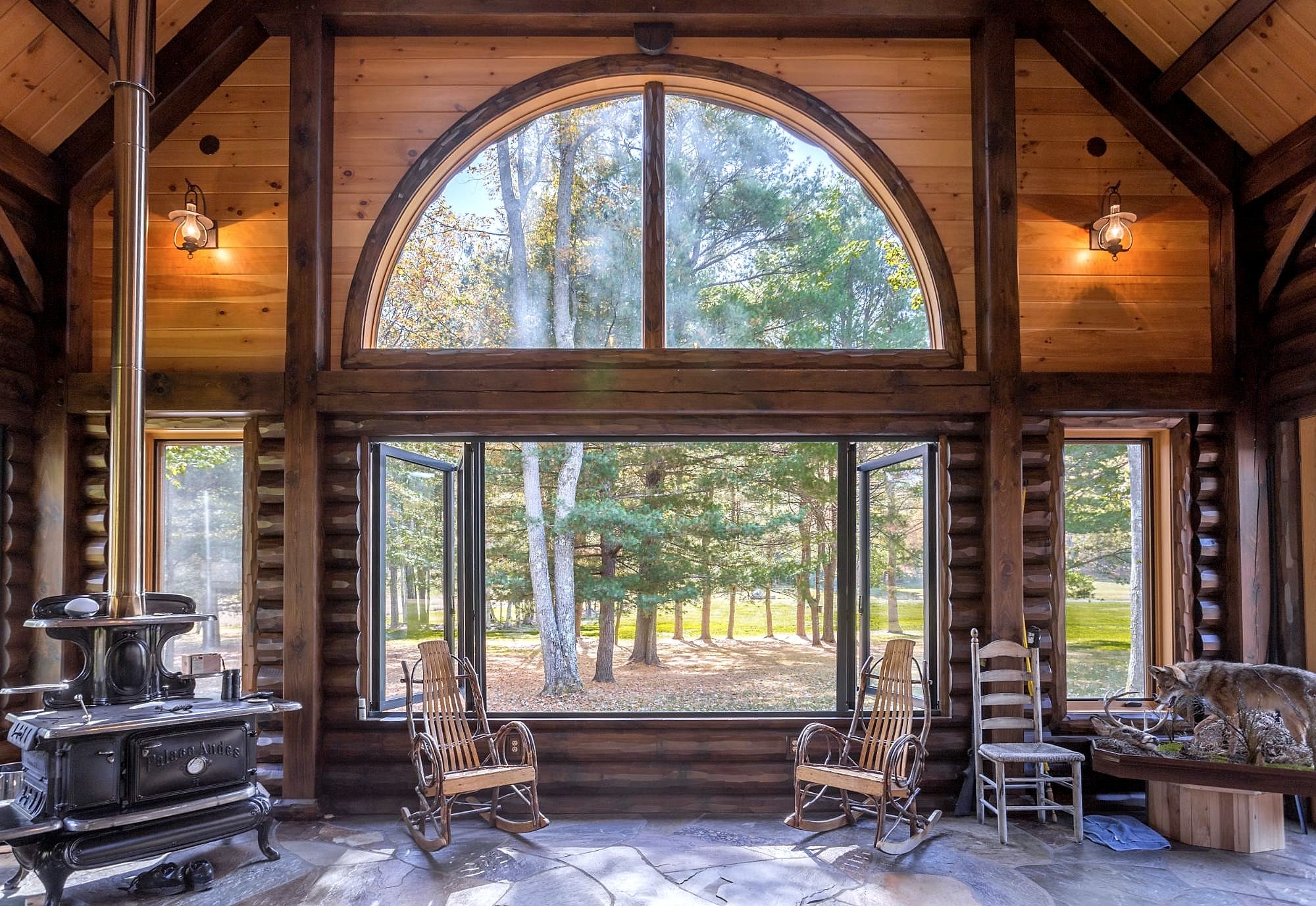 The log-walled room's arched window, the lower windows swung open to the trees