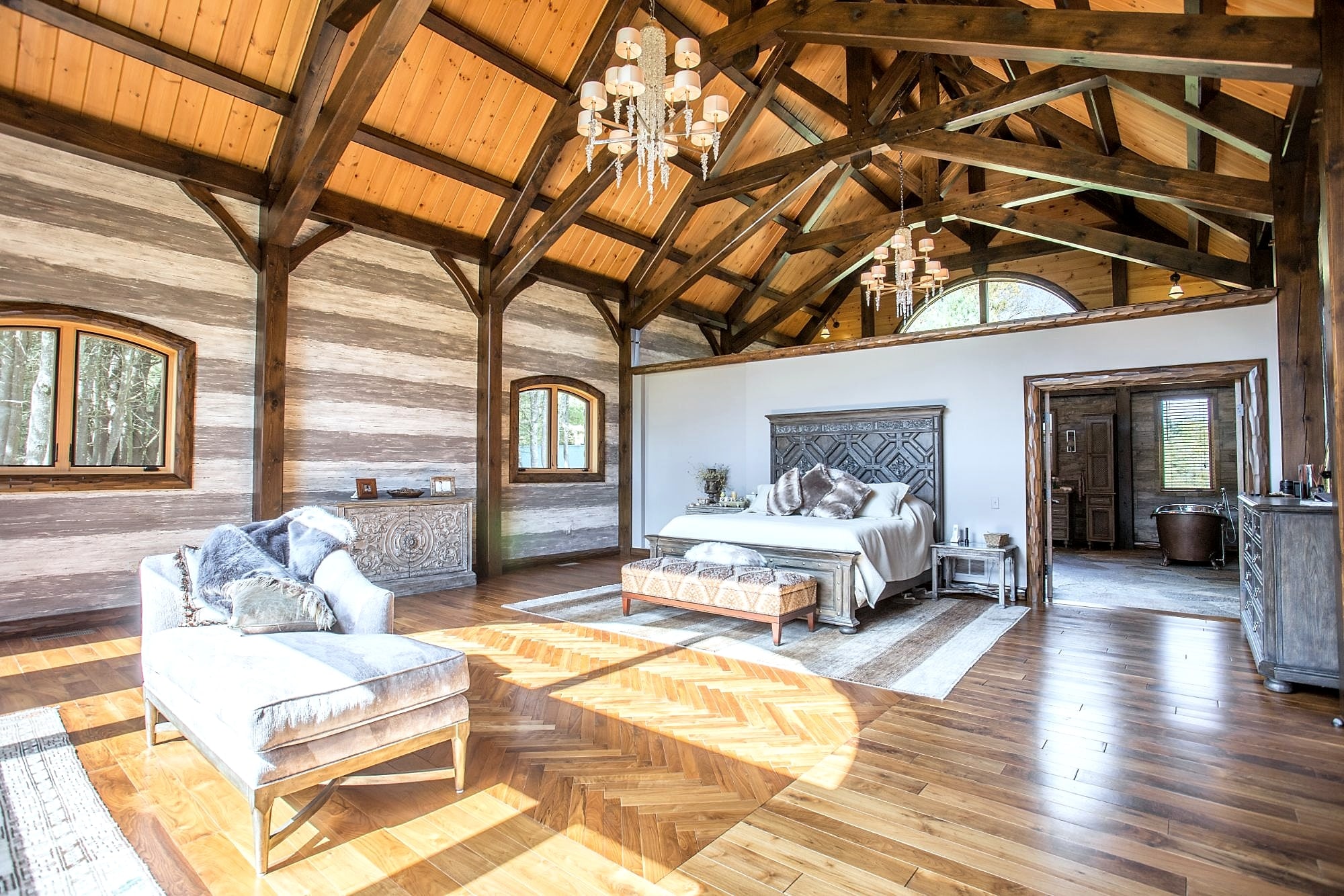 The master suite, wide: chaise, bed, and the bath beyond under one run of trusses