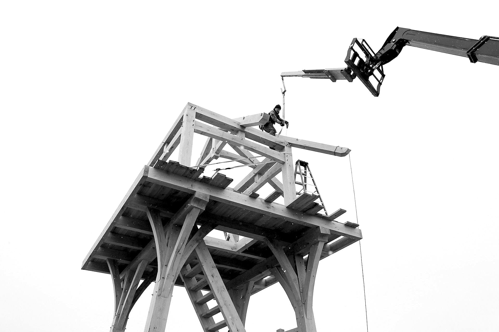 A framer on the top platform setting the roof frame from a telehandler, snow in the air, black and white