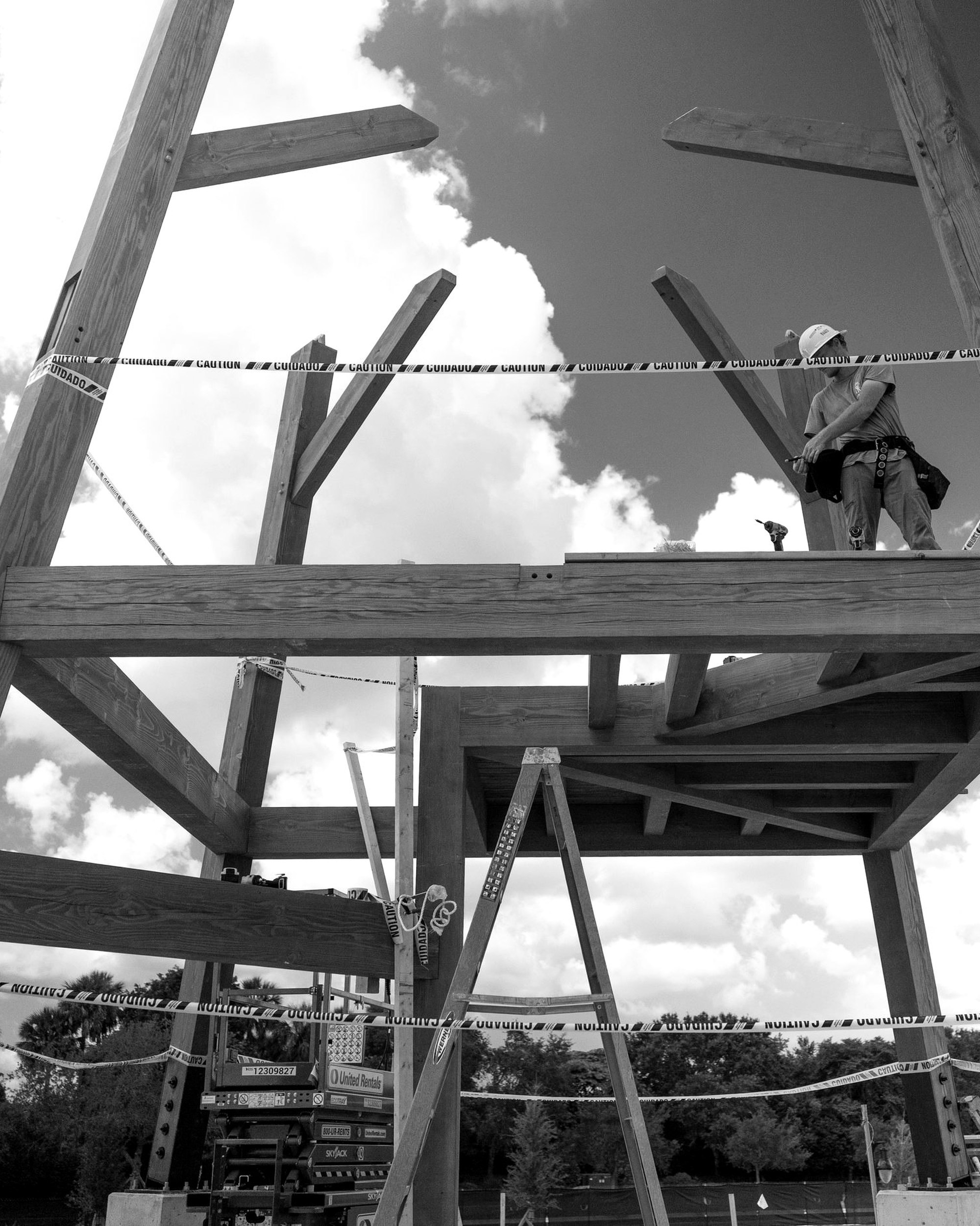 Raising day, in black and white: battered posts and floor framing standing against the sky, crew on the deck