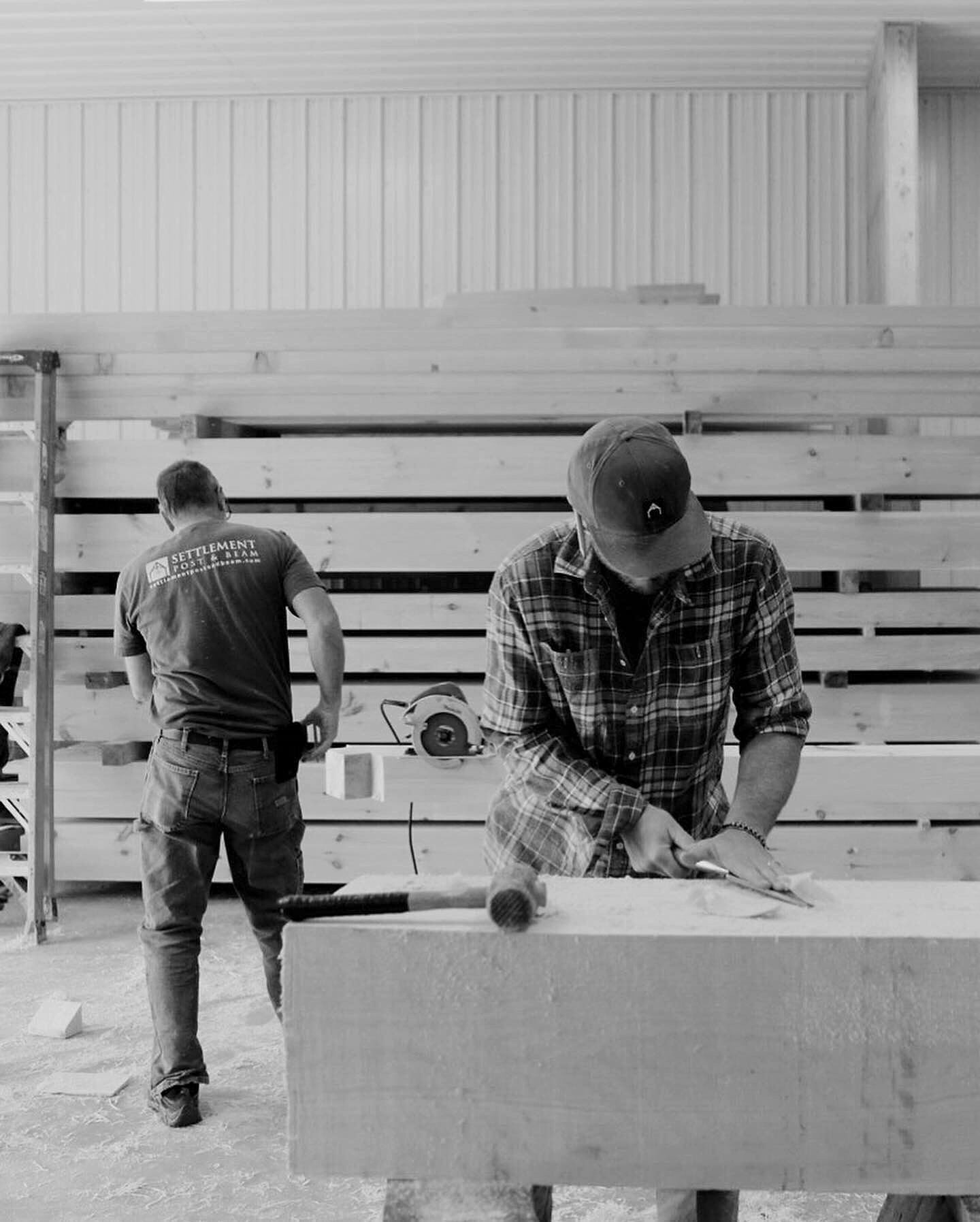 Two framers at the bench, one paring a timber with a chisel