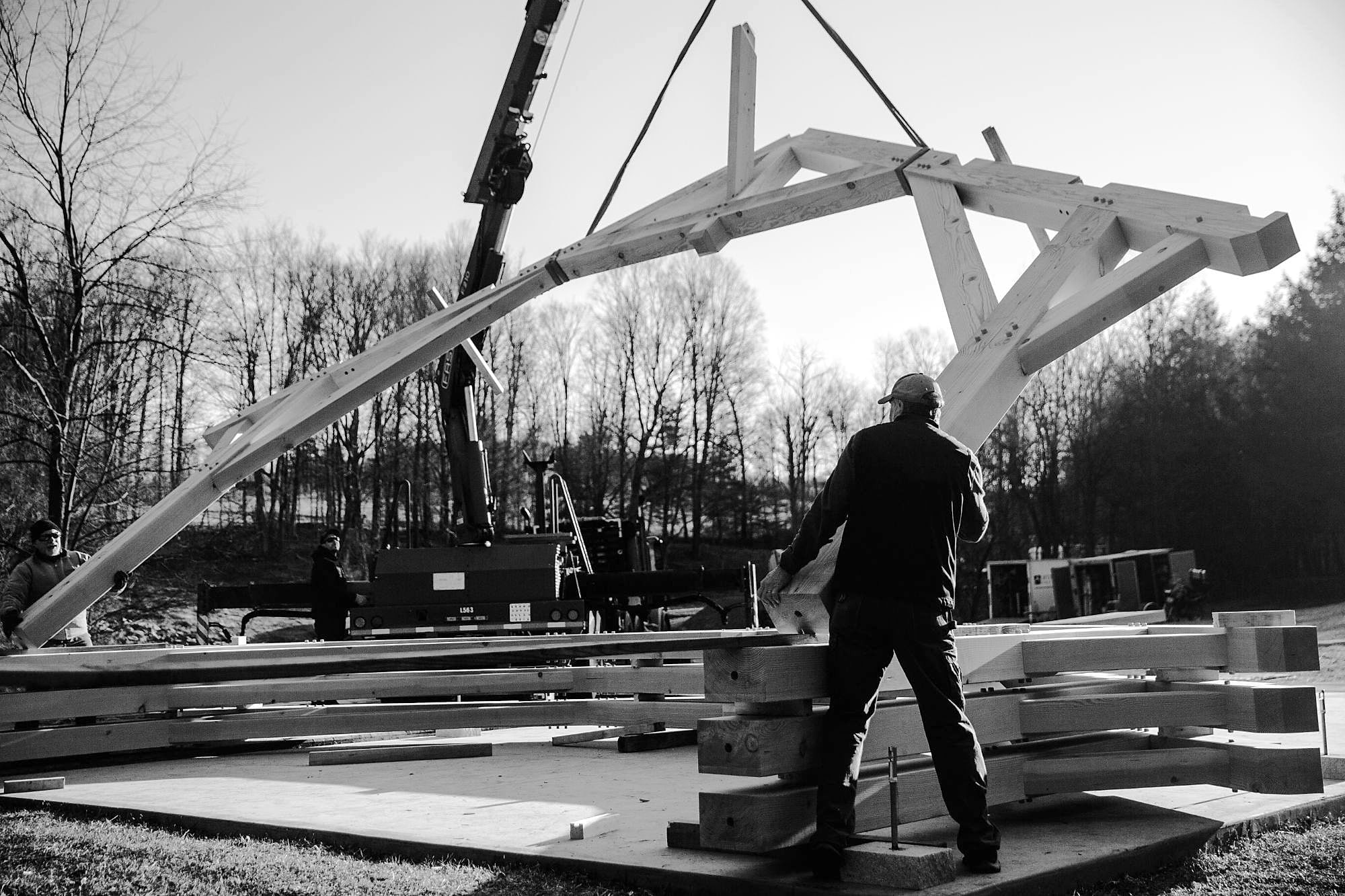 A crane lifting a truss off the stack, Greg guiding it from the deck
