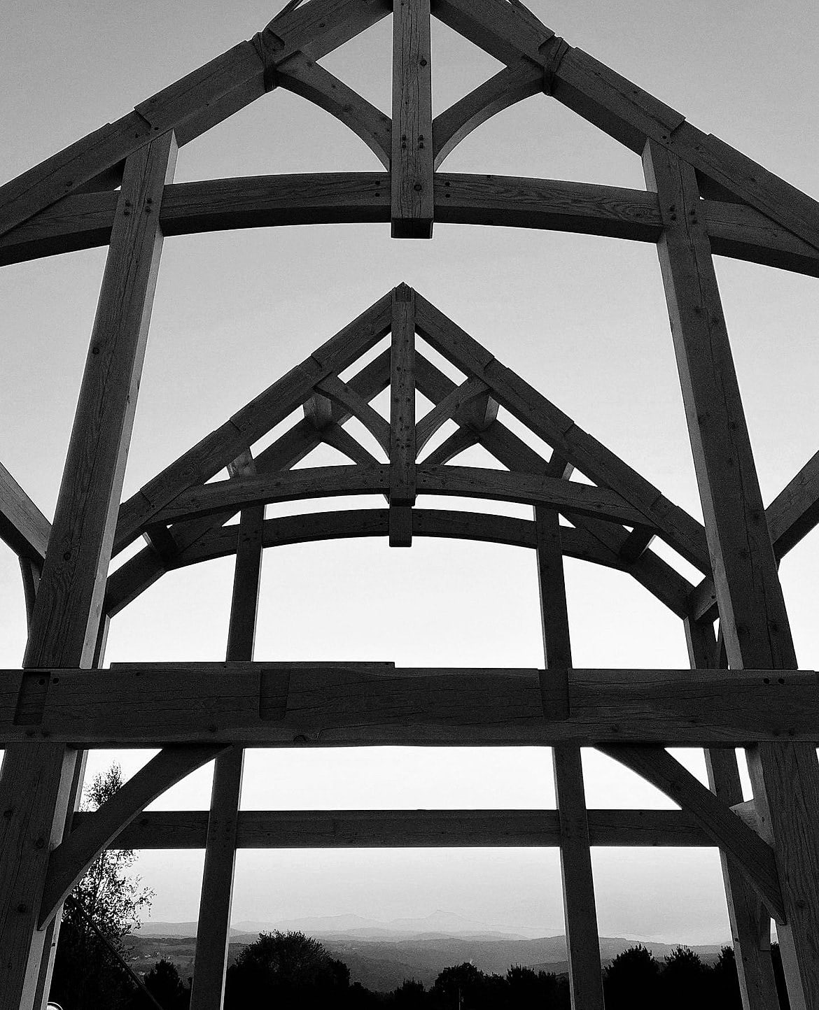 A hammer beam frame at the end of raising day, hills and a sunset through it