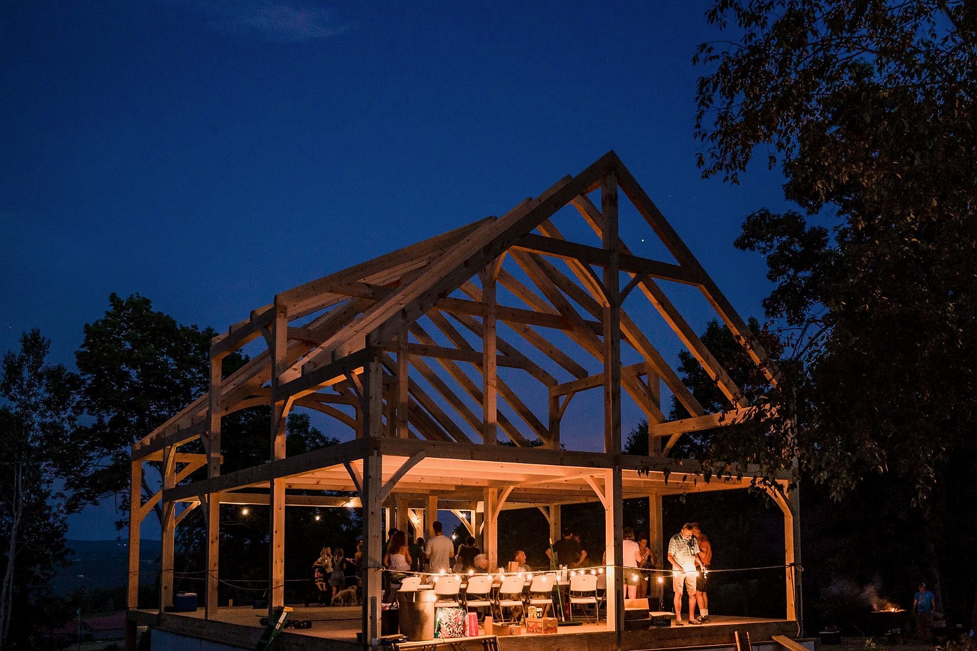 The raising party: a table and string lights under the new frame at night, the crew and the owners around it