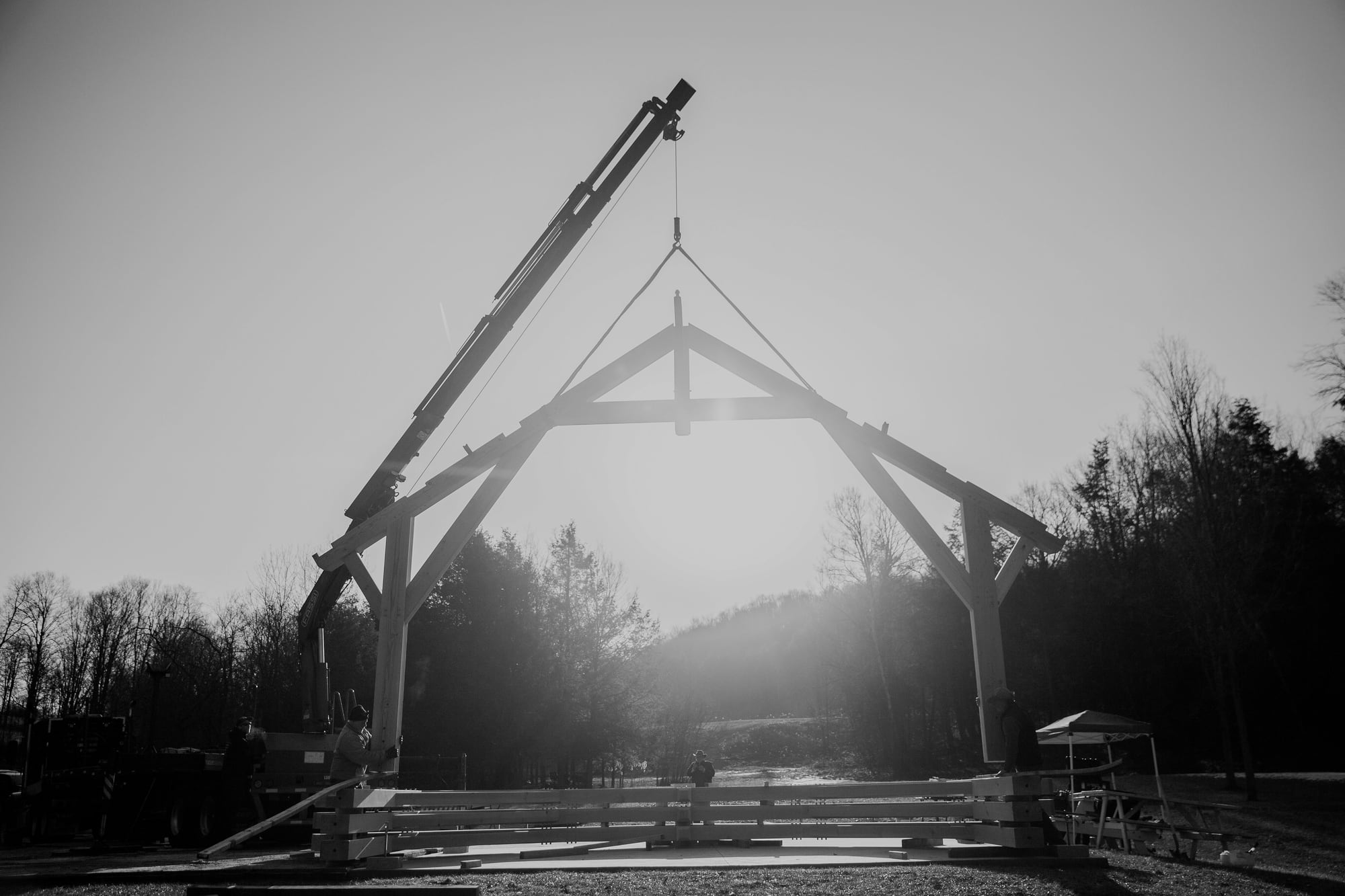 A bent hanging from the crane against the low sun, the crew at its feet, black and white