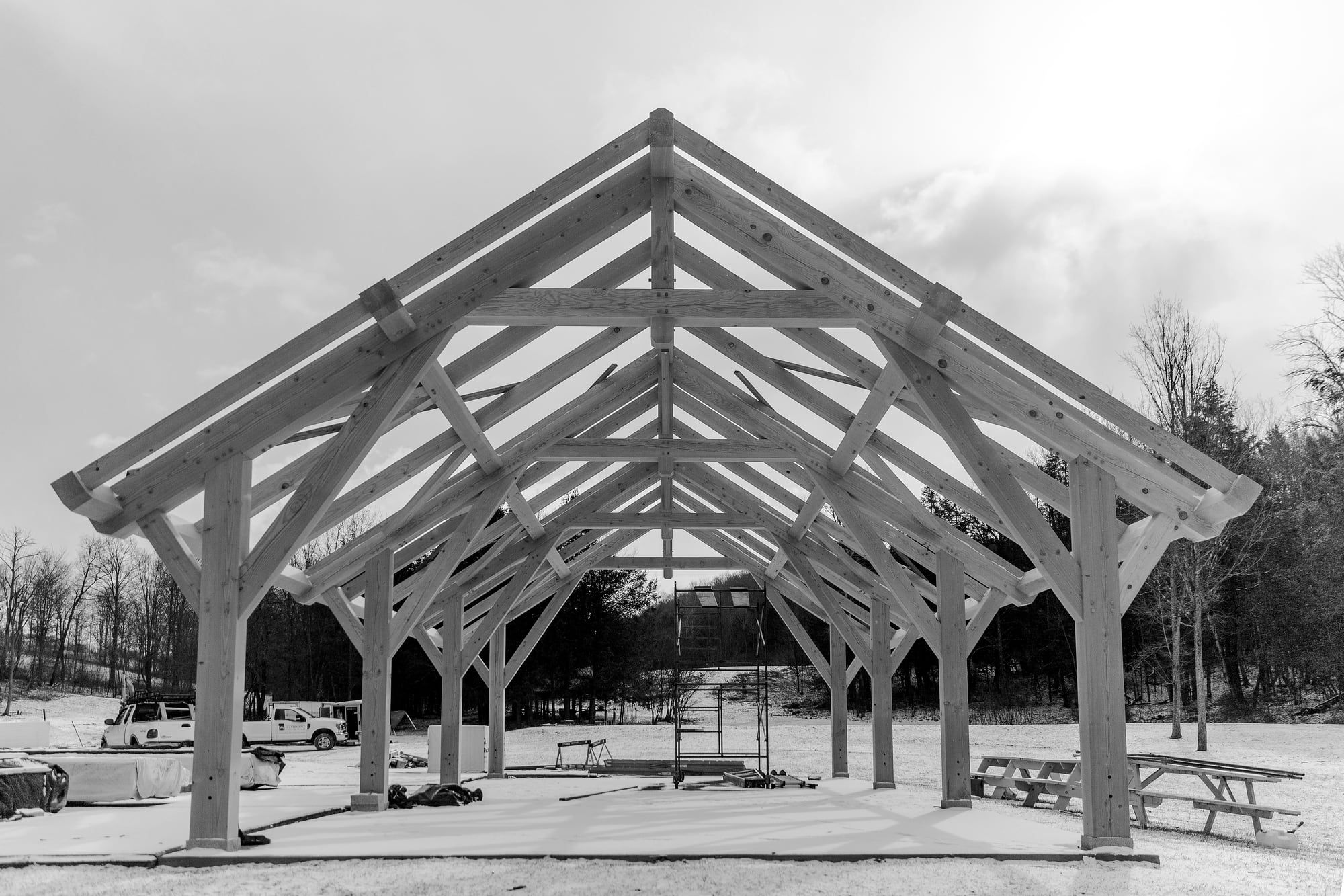 The finished Douglas fir frame standing in the snow, trusses and braces open to the sky, black and white
