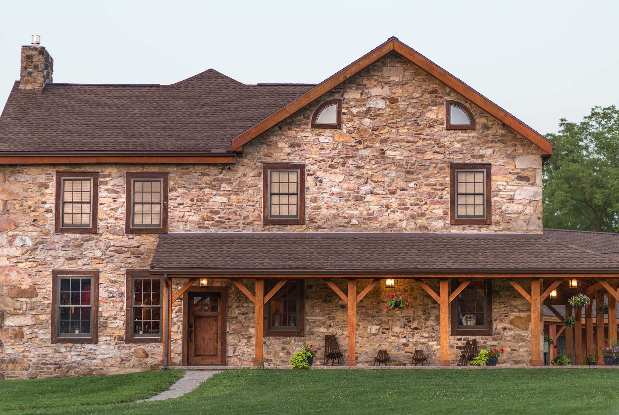 The stone house at dusk, the 1741 datestone in the gable and the timber porch along its front