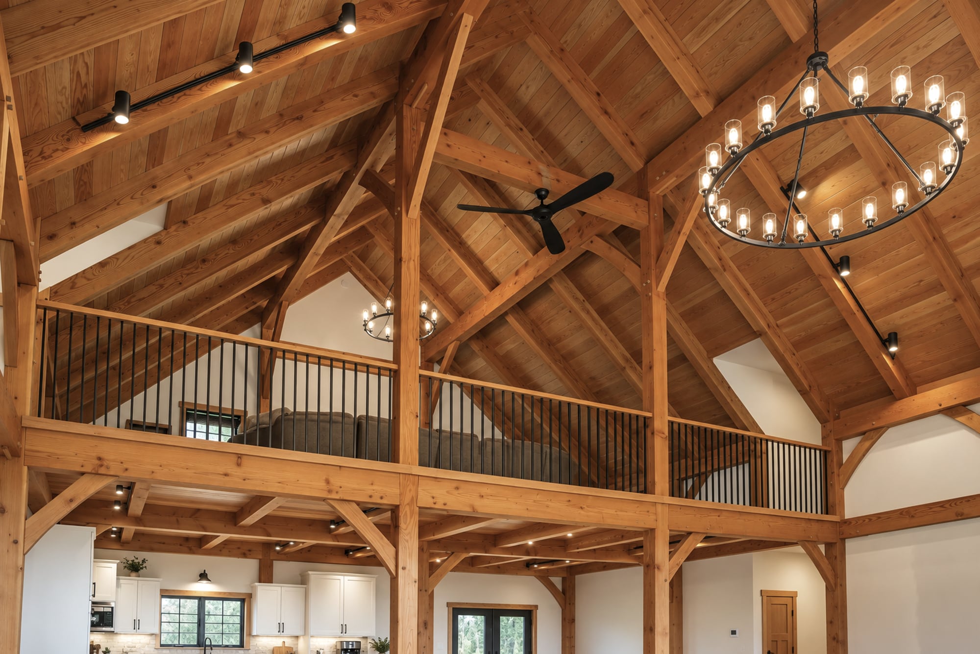 Looking up at the roof frame and the loft rail, a round chandelier hanging in the open bay
