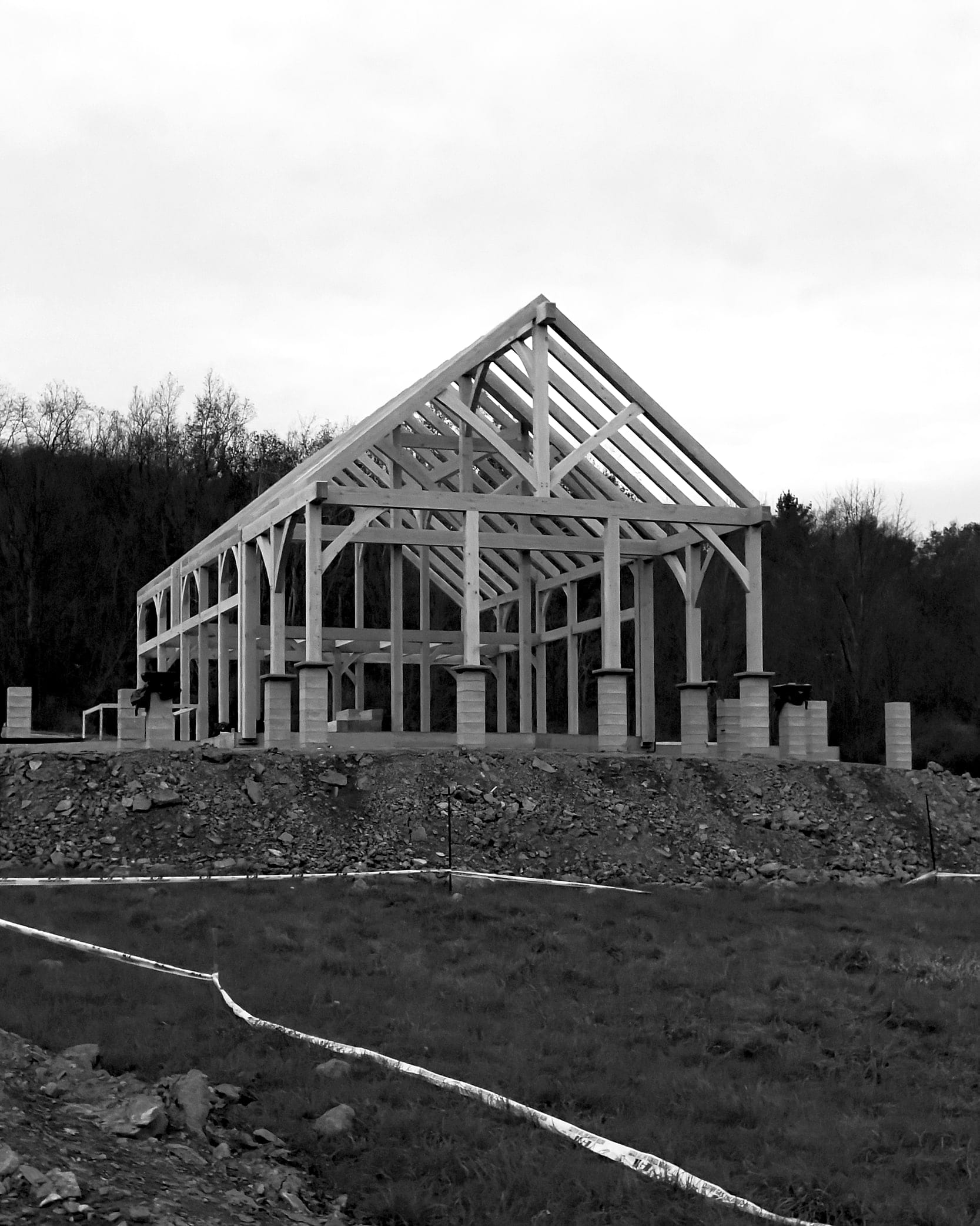 The bare frame standing on its piers on the graded site, black and white