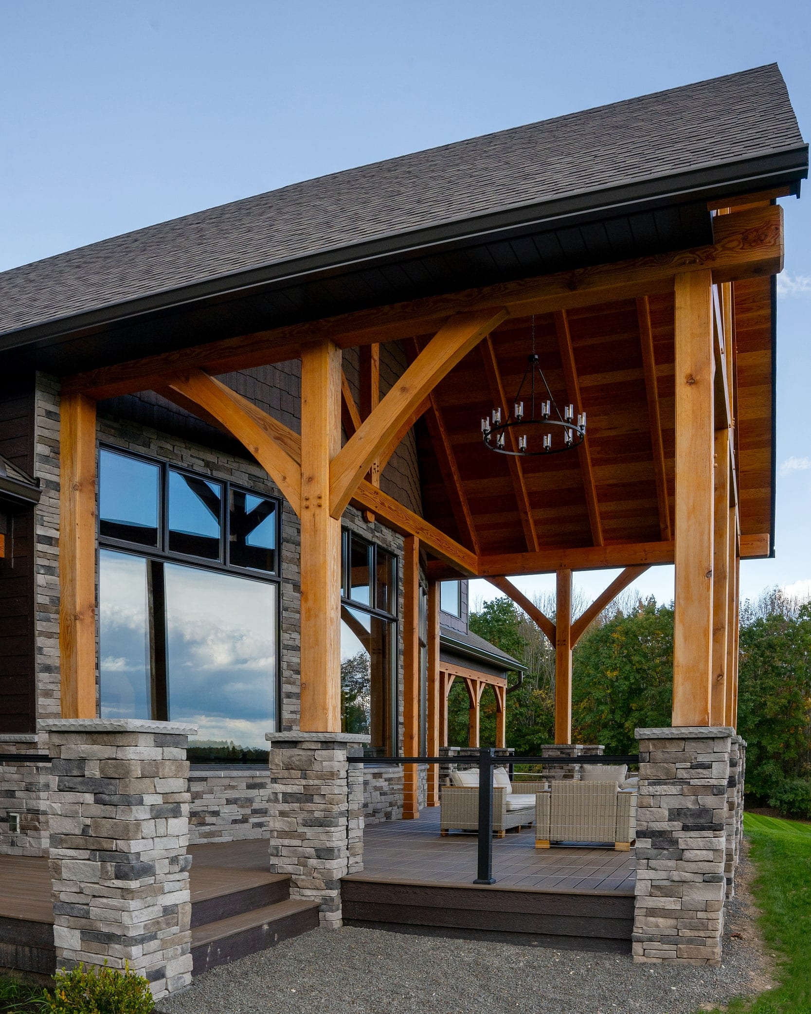 The covered porch: timber posts and curved braces on stone piers, a chandelier under the roof