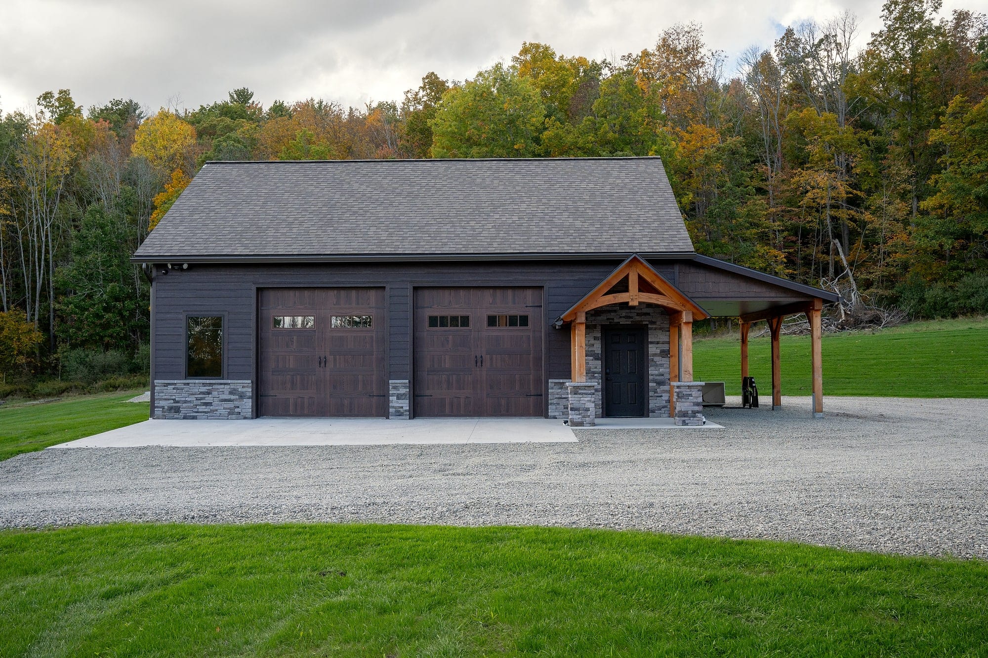 The garage with a small timber gable over its door and an open timber carport beside it