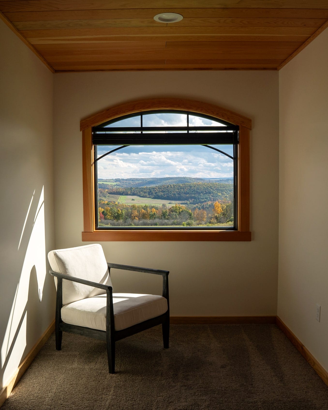 A chair under an arched window looking out over wooded hills and farm fields